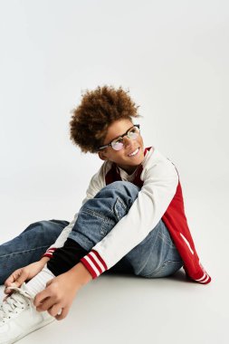 Sevimli küçük çocuk neşeli bir gülümseme ile neşeli bir şekilde oturuyor, moda kıyafetlerini ve tarzını sergiliyor..