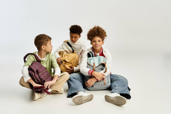 Три очаровательных мальчика в яркой связи в одежде сидя вместе, демонстрируя свою дружбу.