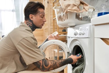 Dövmeli genç adam evde çamaşır yıkarken rahat bir anın tadını çıkarıyor..