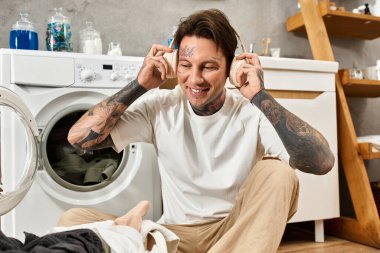 Dövmeleri olan genç bir adam evde rahat rahat otururken müzik dinliyor, kendini rahat hissediyor..