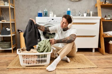 Dövmeli genç adam evde rahat bir günün tadını çıkarırken çamaşırları düzenliyor ve müzik dinliyor..