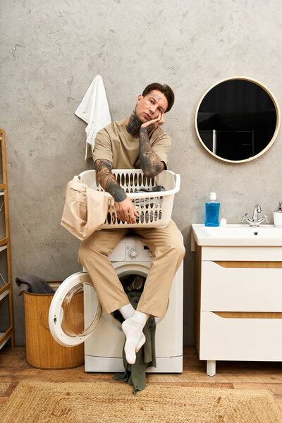 A tattooed young man relaxes on a washing machine in a cozy home while doing laundry.