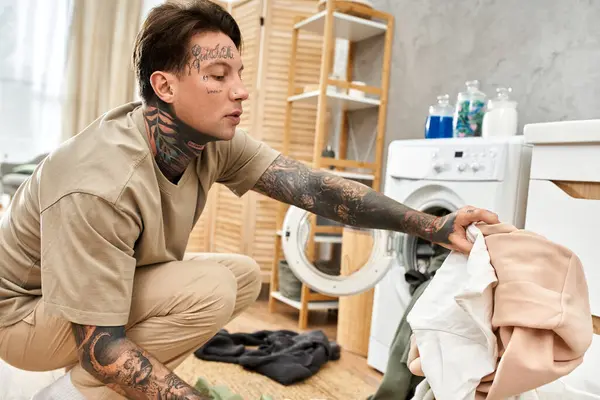 Ev dekorasyonu ve hafif ışıkla çevrili, çamaşırhane işleriyle uğraşan yakışıklı, dövmeli adam..