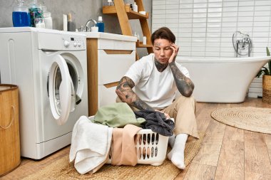 Dövmeli genç bir adam rahat bir banyoda çamaşırlarını yıkarken rahatlıyor..