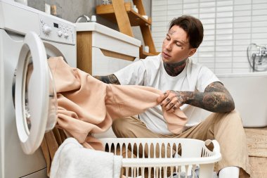 Dövmeleri olan genç bir adam, rahat bir odada otururken çamaşırları sıralamaya odaklanıyor..