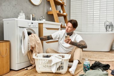 Dövmeli genç bir adam rahat evinde çamaşır yıkarken rahat bir anın tadını çıkarıyor..