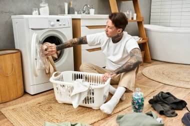 Dövmeli genç bir adam evinde çamaşır işi yapar. Evinde rahat ve stil yayar..