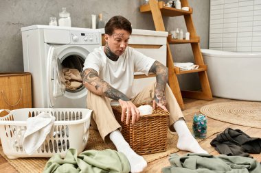 Dövmeli genç adam rahat bir şekilde evinde oturuyor, rahat bir atmosferde giysilerini katlıyor..