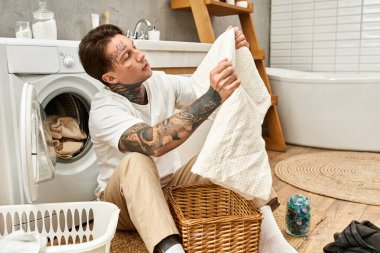 Dövmeleri olan rahat bir genç adam evinde çamaşırlarını katlıyor ve rahat bir ortam yaratıyor..