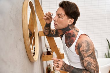 Dövmeleri olan genç bir adam rahat bir evde cilt bakımına odaklanır..