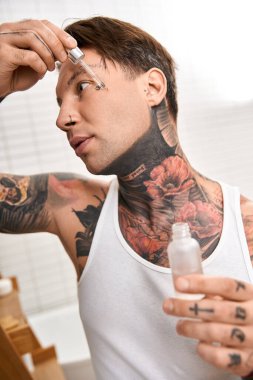 Karmaşık dövmeleri olan genç bir adam evinde rahat bir anın tadını çıkarırken cildine serum sürüyor..