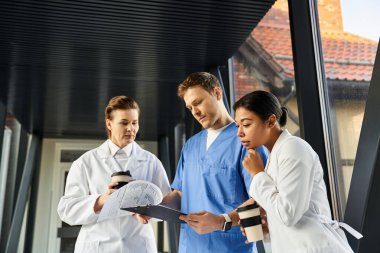 Three diverse medical professionals share crucial patient information in a hospital corridor.