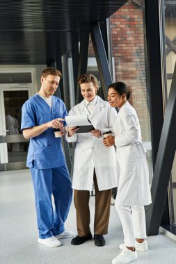 Three diverse doctors discuss plans in a hospital corridor.
