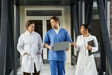 Three doctors engage in a discussion while walking through a sleek hospital corridor.