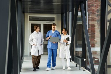 Three multicultural doctors discuss patient information in a sleek hospital setting.