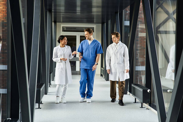 A Black woman and two doctors chat animatedly while walking down a hospital corridor.
