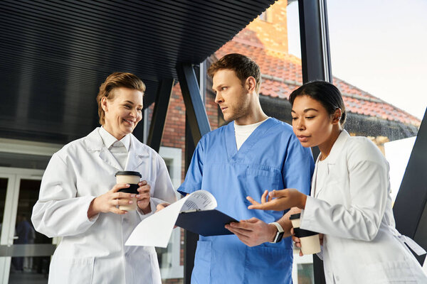 Three diverse medical experts collaborate in a modern hospital, exchanging insights.
