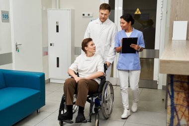 A skilled doctor and a compassionate nurse assist a female patient in a wheelchair.