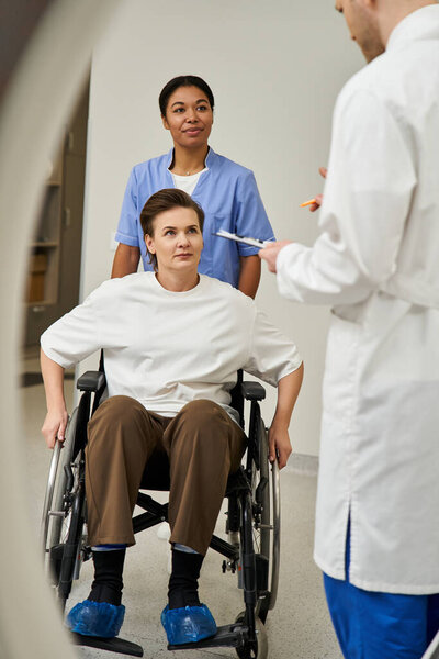 Dedicated doctor and nurse prepare female patient in wheelchair for MRI in a contemporary hospital.