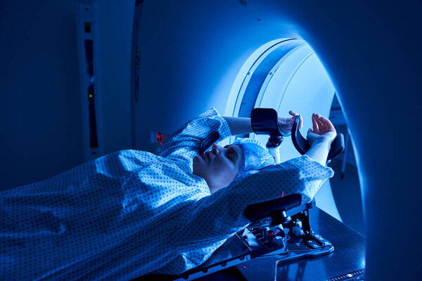 A woman lies in an MRI machine, surrounded by a tranquil blue ambiance, in a contemporary hospital.