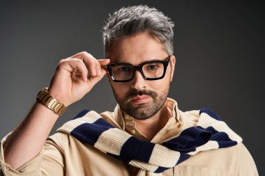 Yakışıklı bir adam şık kıyafetlerini ve gözlüklerini stüdyoda rahatça poz verirken sergiliyor..