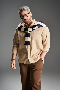 Gözlüklü şık bir adam şık bir stüdyoda kendine güvenerek poz veriyor, zarafet ve karizma yayıyor..