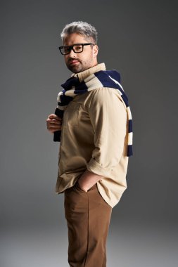 Gözlüklü bir adam şık poz veriyor, modern bir stüdyoda şık bir kıyafet sergiliyor..