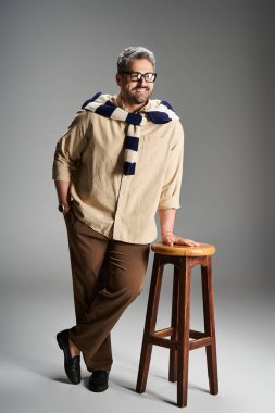 Gözlüklü yakışıklı bir adam şık kıyafetlerini iyi aydınlatılmış bir stüdyoda poz verirken sergiliyor..