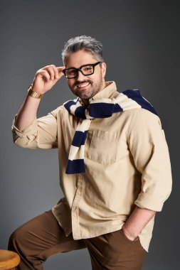 Gözlüklü yakışıklı, şık giyinmiş, stüdyo ortamında kendine güveni olan bir adam..