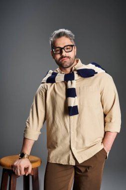 Gözlüklü şık bir adam stüdyoda kendine güvenerek duruyor, zarafet saçıyor..