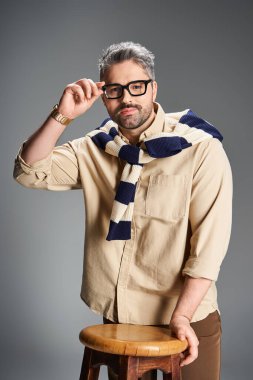 Yakışıklı bir adam gözlüğünü sofistike bir stüdyoda ayarlarken modaya uygun kıyafetlerini sergiliyor..