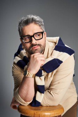 Modaya uygun bir adam şık bir stüdyoda gözlüklü şık bir kıyafetle düşünceli bir şekilde poz verir..