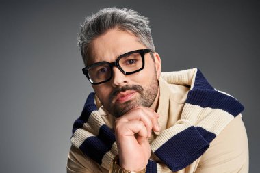 Gözlüklü kendine güvenen bir adam şık kıyafetini gösterişli bir arkaplanda sergiliyor..