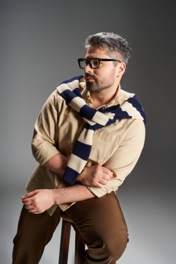 Moda kıyafetli yakışıklı bir adam stüdyo ışıkları altında rahatça poz verir..