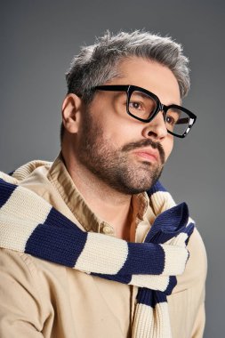 Şık bir adam şık bir kıyafeti ve çarpıcı gözlükleriyle bir stüdyoda zarafetini sergiliyor..