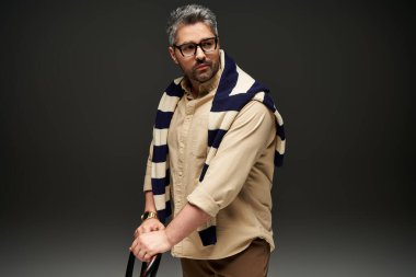 Gözlüklü şık adam zarif poz veriyor, şık kıyafetini ve kendine güvenini vurguluyor..