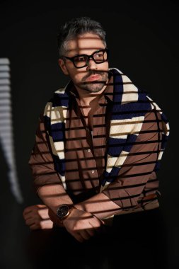 Gözlüklü şık bir adam kendine güvenen bir poz verir. Stüdyoda şık bir kıyafet giyer..