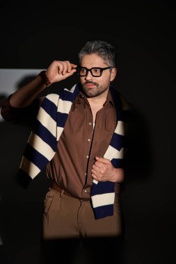 Yakışıklı bir adam şık bir kıyafetin içinde özgüvenle poz veriyor. Stüdyo ışıklarının altında modaya uygun bir cazibe yayıyor..