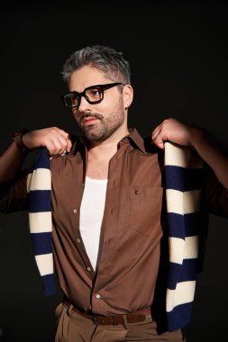 Gözlüklü yakışıklı, modern bir stüdyo ortamında modaya uygun bir şekilde poz veriyor..