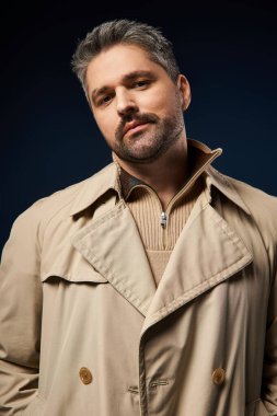 Yakışıklı bir adam modern bir stüdyoda karanlık bir arkaplan karşısında şık kıyafetini sergiliyor..