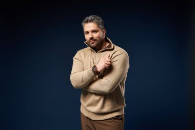 Moda kıyafetleri giymiş yakışıklı bir adam, karanlık bir arkaplanda rahatça poz veriyor..