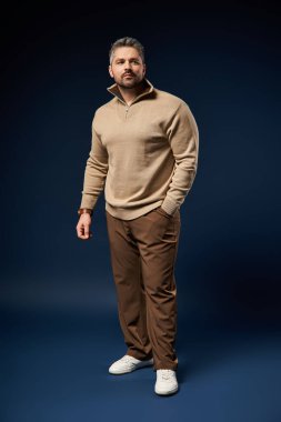 Kendine güvenen bir adam modaya uygun bir süveter ve pantolon giyer, stüdyoda moda ve karizma yayar..