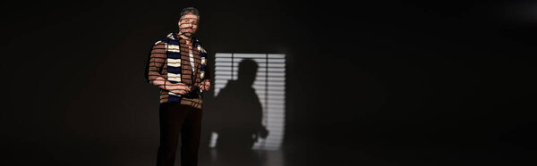 A confident man showcases his trendy outfit in a stylish studio, illuminated by striking lighting, banner