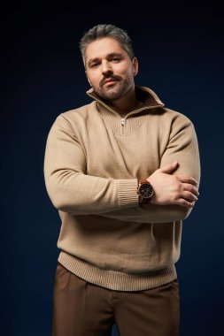 Tüylü, kendine güvenen bir adam şık bir kıyafet içinde stüdyo ortamında moda yayıyor..