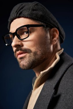 Gözlük takan yakışıklı adam, şık ve şık bir elbiseyle karanlık bir arkaplanda rahatça poz veriyor..