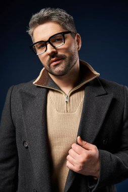 Adam kendine güveni tam bir şekilde şık elbisesiyle karanlık bir arkaplanda poz veriyor..