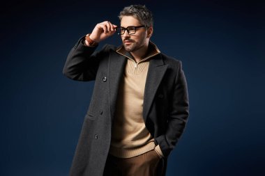 Gözlüklü yakışıklı bir adam stüdyoda kendine güveni olan şık kıyafetini sergiliyor..