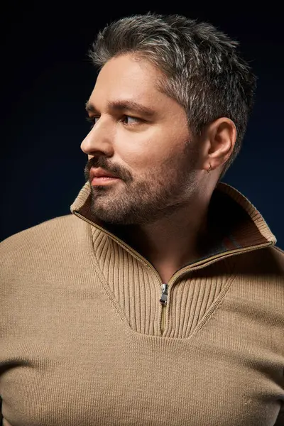 Tüylü adam özgüvenle poz veriyor, moda tercihlerini bir stüdyo arkaplanında vurguluyor.