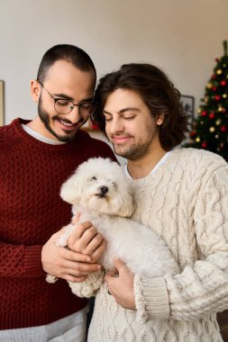İki adam evde sıcak bir anı paylaşıyor, tüylü bir köpeği tutarken sevgilerini kucaklıyorlar..