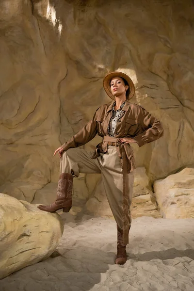 Junge Archäologin in Safari-Kleidung und Cowboystiefeln posiert in der Wüste in der Nähe von Steinen — Stockfoto